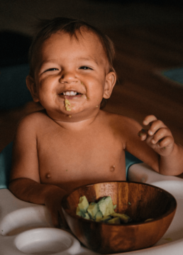 Bébé en train de manger des légumes dans un bol sur une chaise haute souriant