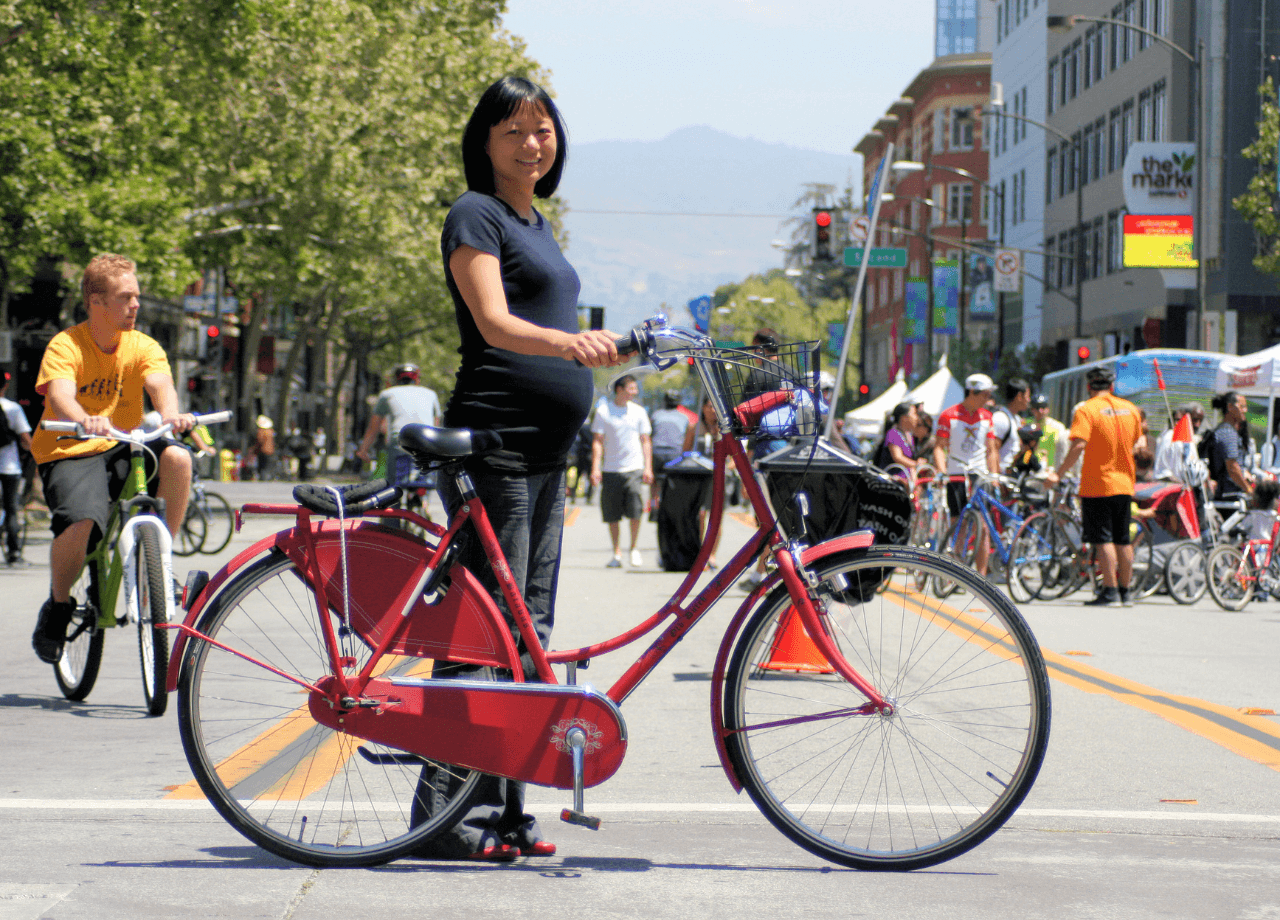 Femme enceinte souriante avec un vélo rouge sur la route