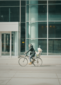 Maman à vélo et son bébé dans un siège vélo devant un bâtiment