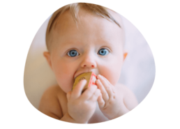 Bébé avec des grands yeux bleus regardant la caméra avec un cube entre les mains et la bouche