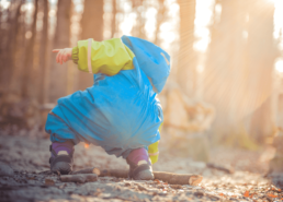 Enfant en tenue bleu et verte ramasse un bout de bois dans la nature